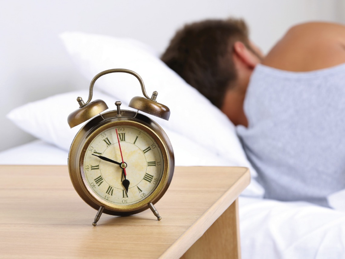 an alarm clock with man sleeping in background