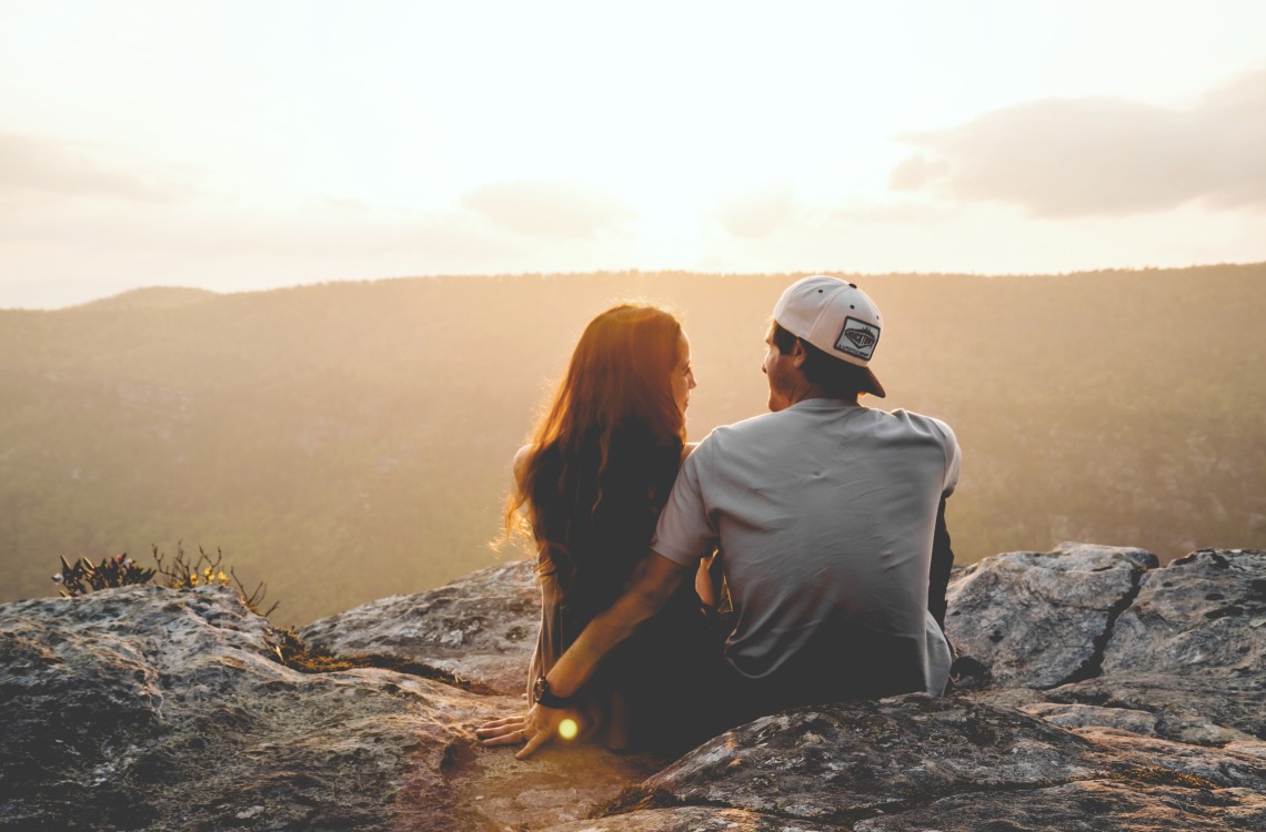 Two people sittng on a rock talking overlooking wilderness